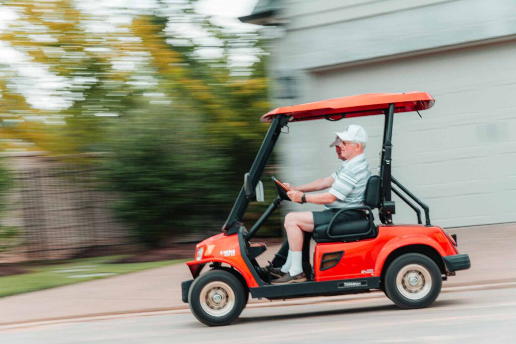 Senior men ride in a golf cart down a neighborhood street