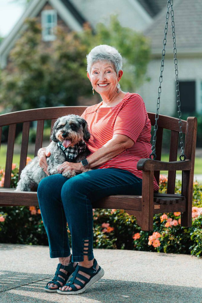 A senior woman sits with their dog on a swinging bench