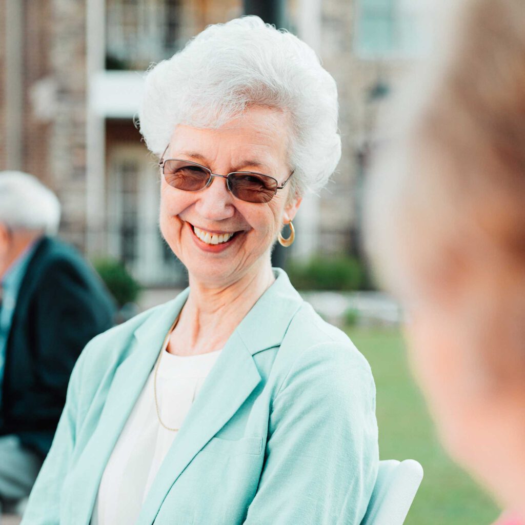 A senior woman with dark glasses smiles to friend while outdoors
