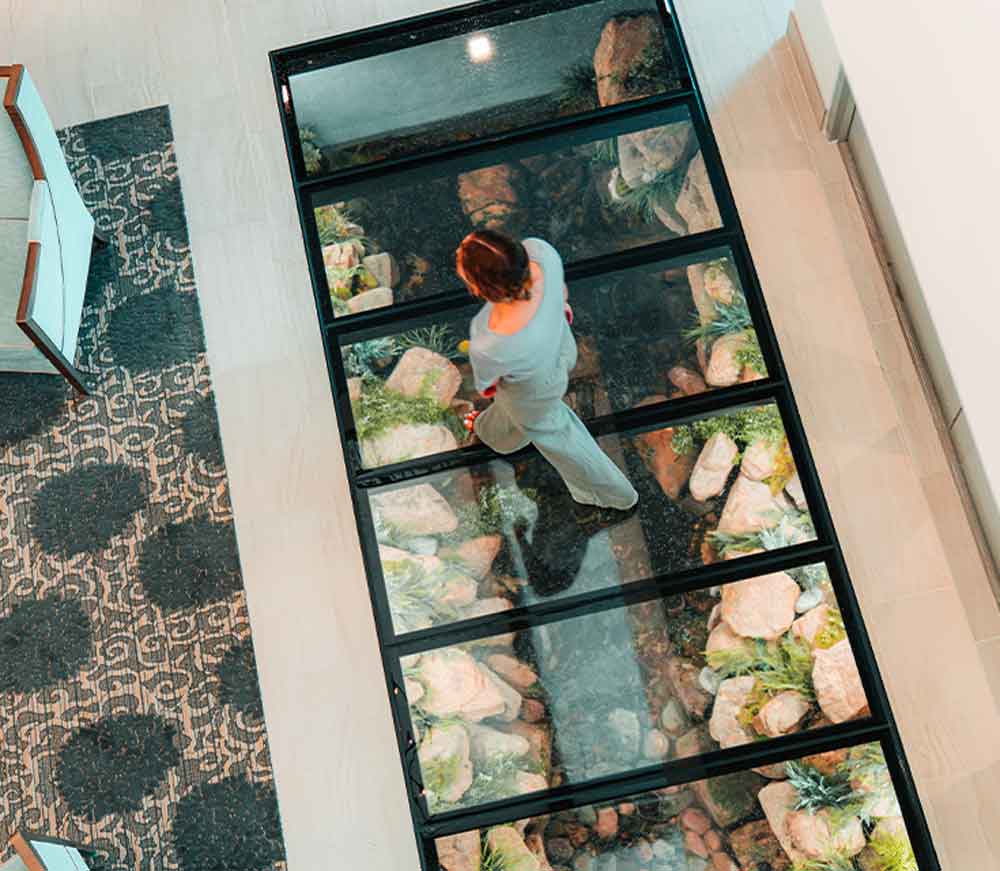 A woman walks over a glass floor above an embedded architectural water feature