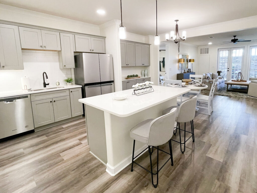 A modern kitchen in an open-concept apartment layout, featuring stainless steel appliances, a large kitchen island, and durable flooring