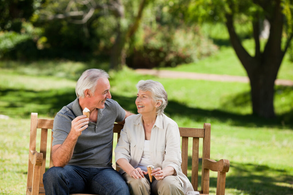 Older couple eating ice cream on a park bench